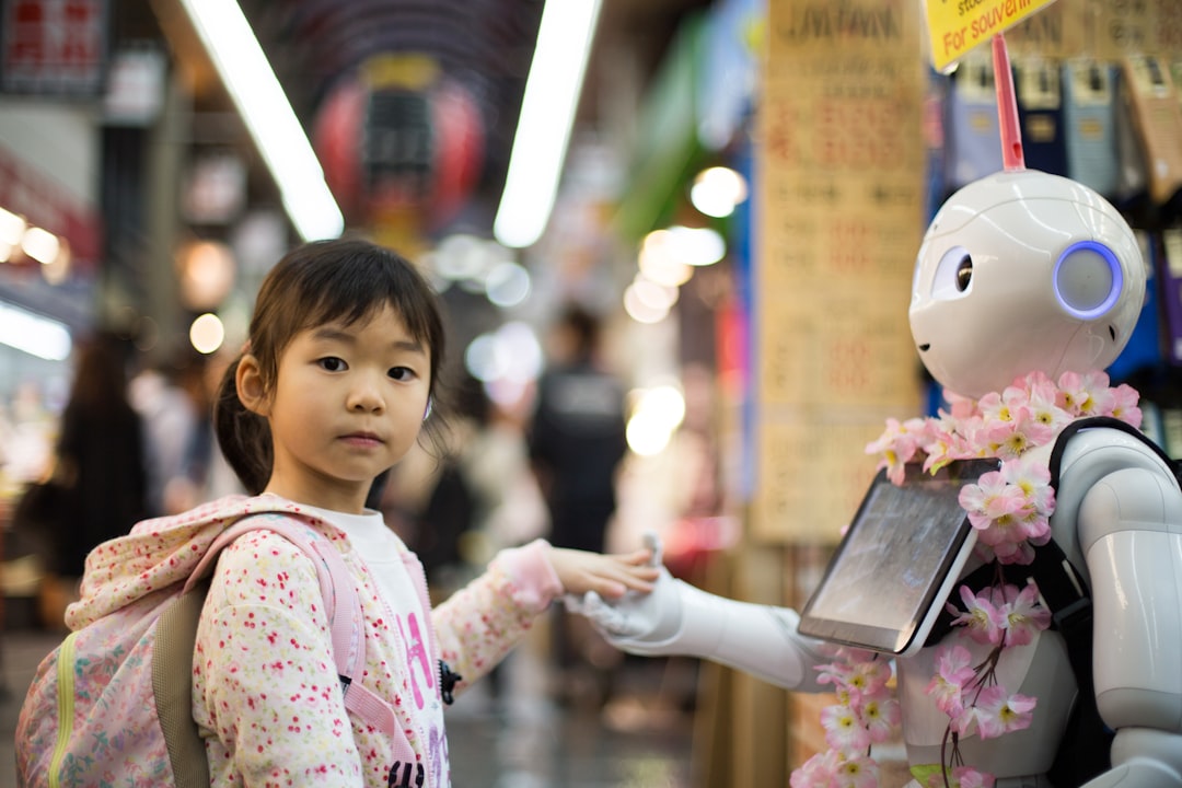 As Kuromon Market in Osaka was about to close for the evening I sampled some delicious king crab and did a final lap of the market when I stumbled upon one of the most Japanese scenes I could possibly imagine, a little girl, making friends with a robot. by Robotic Coding photo of girl laying left hand on white digital robot