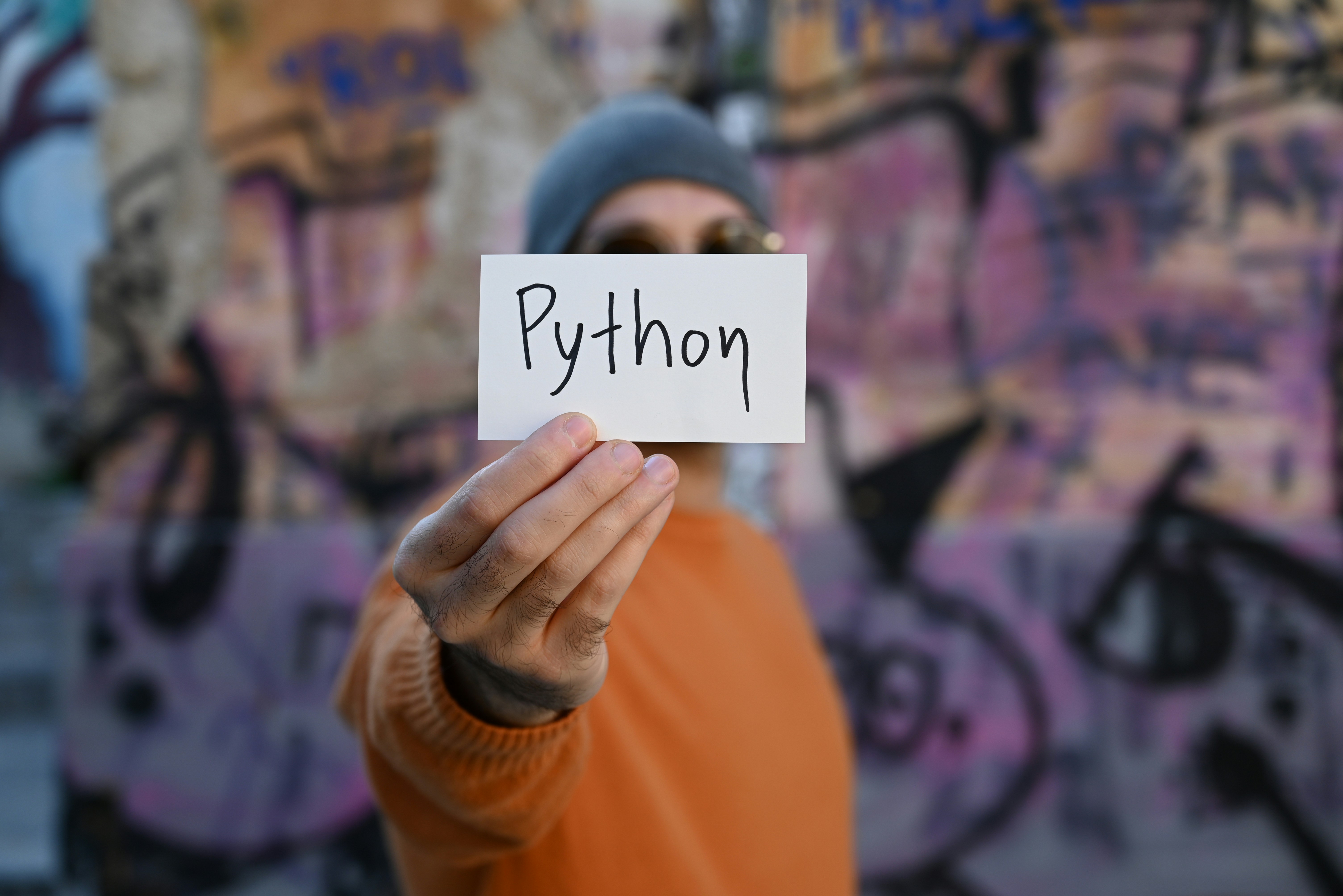Python Programming Language by Robotic Coding a man holding up a piece of paper with the word python written on it